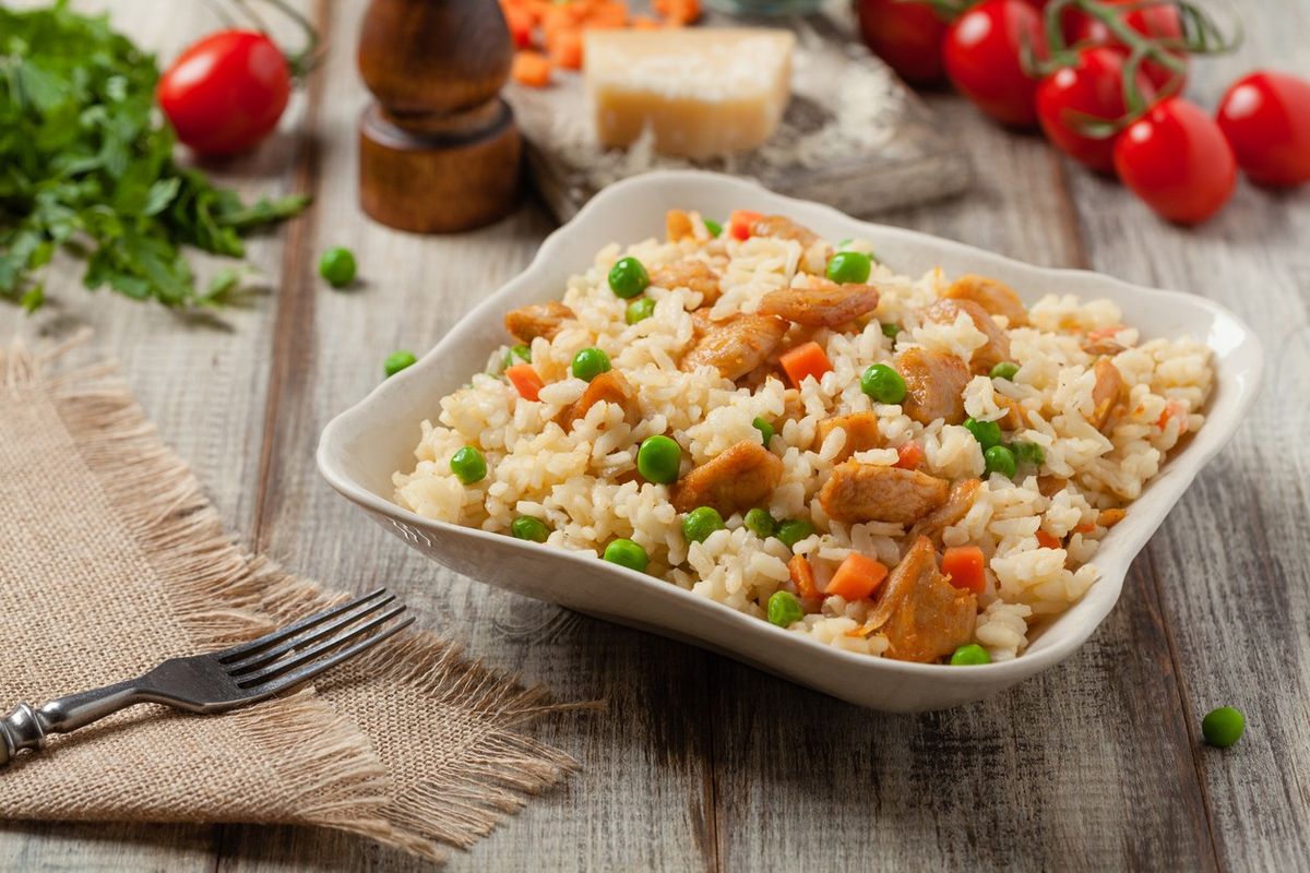 Bowl of chicken and vegetable rice with peas and carrots on rustic wooden table
