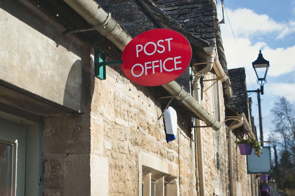 Building exterior showing a red post office sign in a rural village in England 