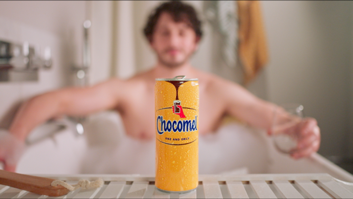 Chocomel advert shows person enjoying chocolate milk alone in bathtub, smiling.