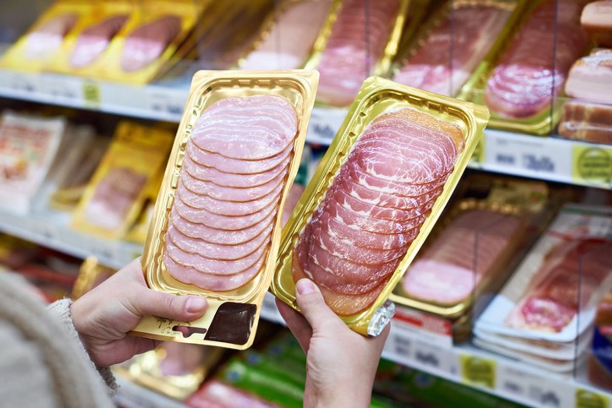 Customer comparing two packs of sliced ham in a supermarket chilled meat section