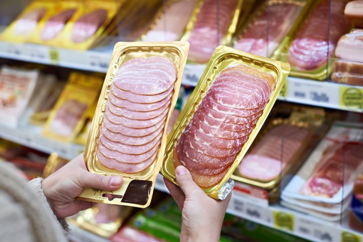 Customer comparing two packs of sliced ham in a supermarket chilled meat section