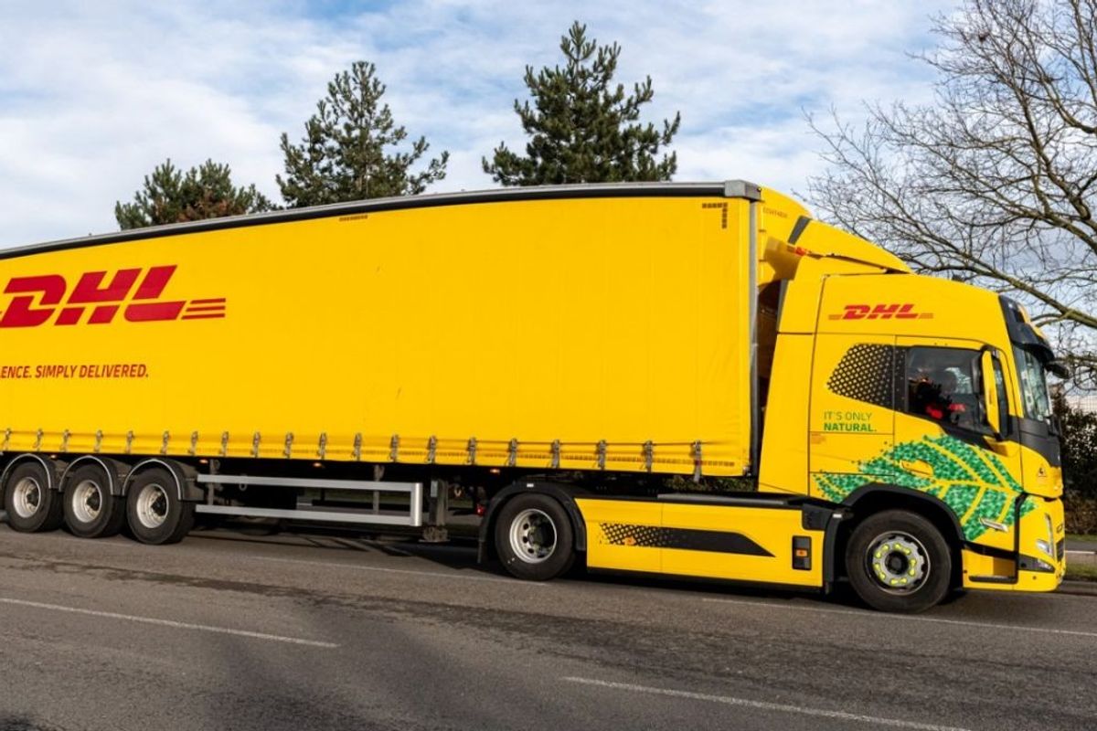 DHL delivery truck parked on roadside, showcasing yellow branded trailer and sustainability graphics on cab.