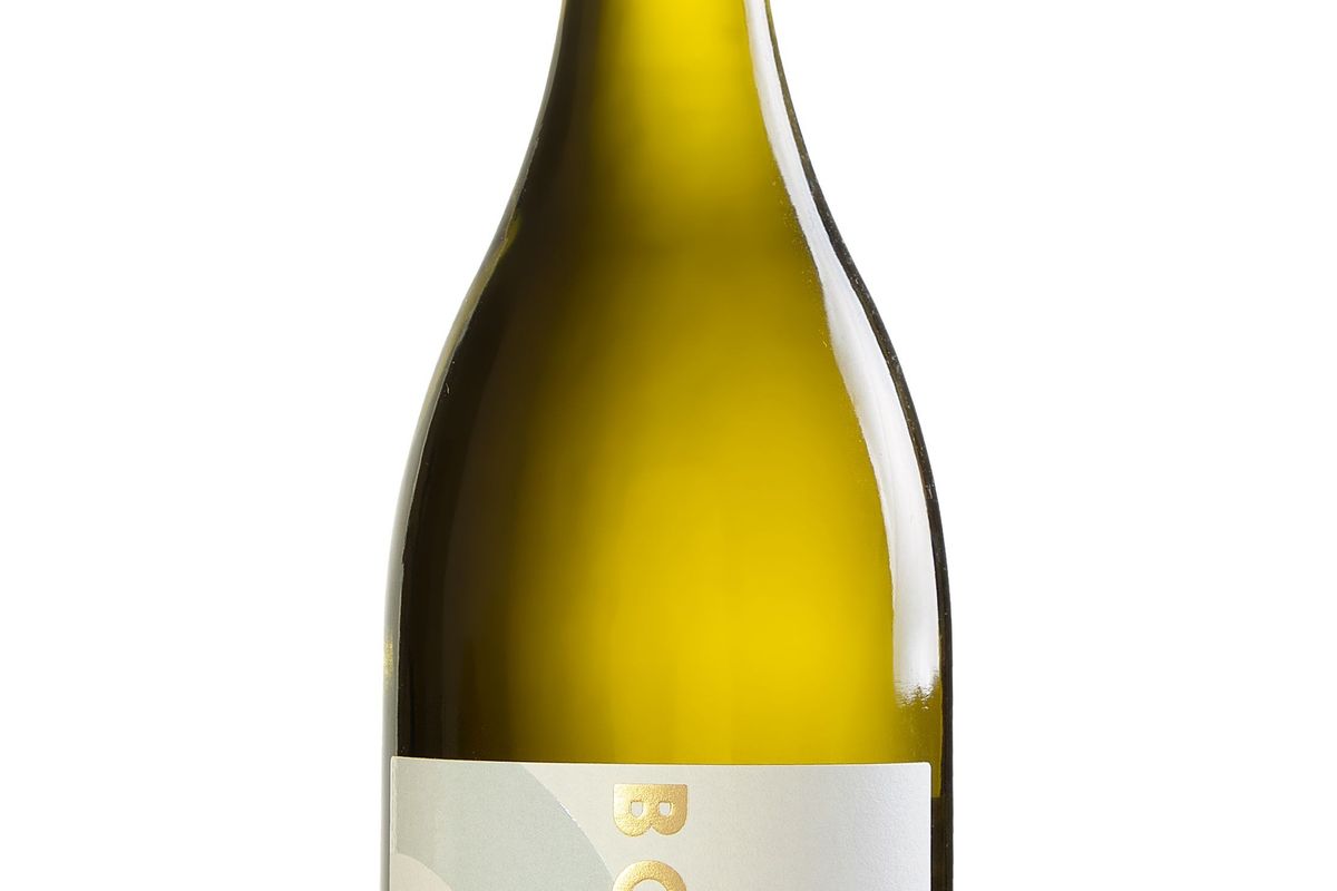 Golden-colored non-alcoholic Chardonnay wine in a glass with grape vines in background