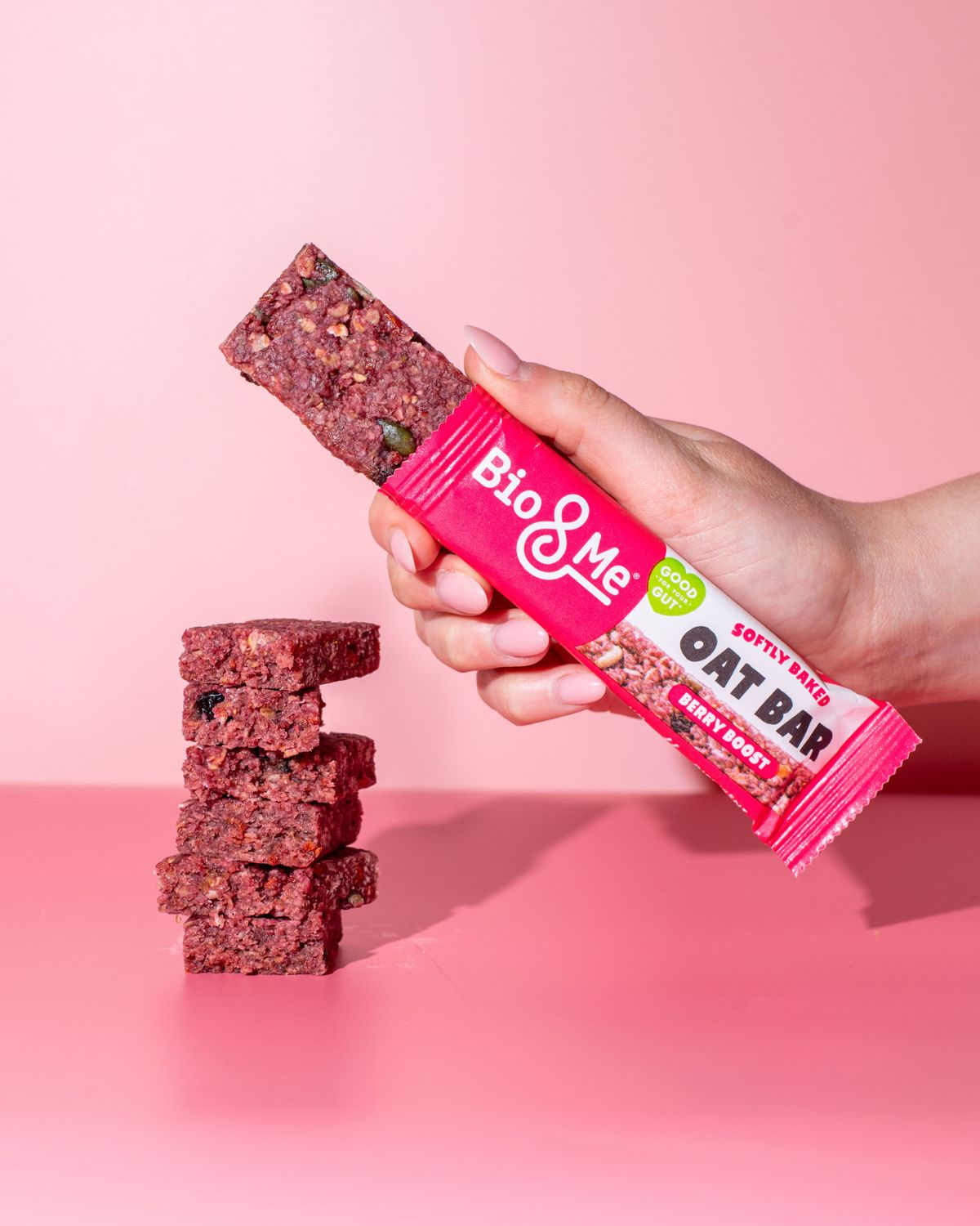 Hand holding Bio&Me Berry Boost oat bar with stacked bars on pink background
