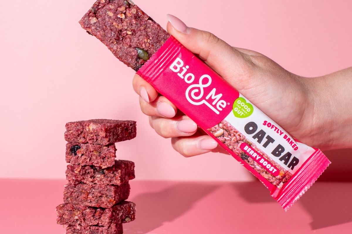 Hand holding Bio&Me Berry Boost oat bar with stacked bars on pink background