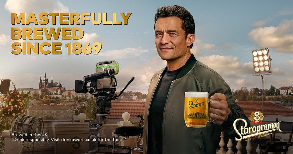 Orlando Bloom holds Staropramen beer on Prague film set with camera.