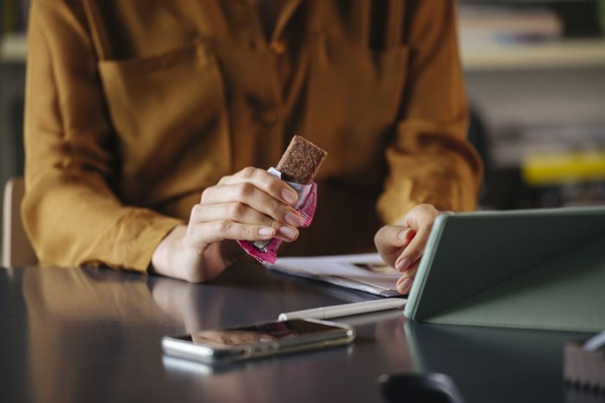 Person unwrapping and eating a chocolate bar while working at a desk on a tablet