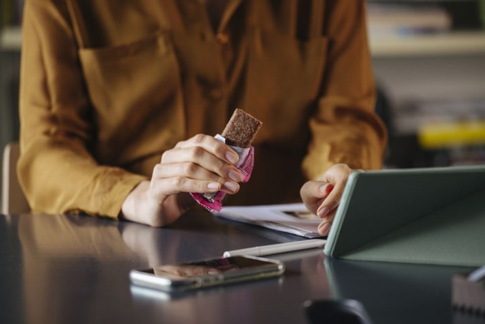 Person unwrapping and eating a chocolate bar while working at a desk on a tablet