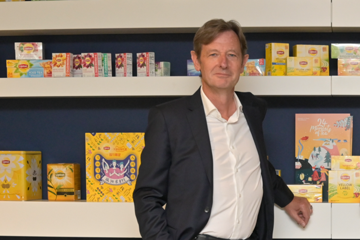 Pierre Laubies, newly appointed CEO of Lipton Teas and Infusions in 2025, stands in a suit in front of shelves displaying Lipton tea products, including Yellow Label and various flavors, highlighting the company’s global tea portfolio.