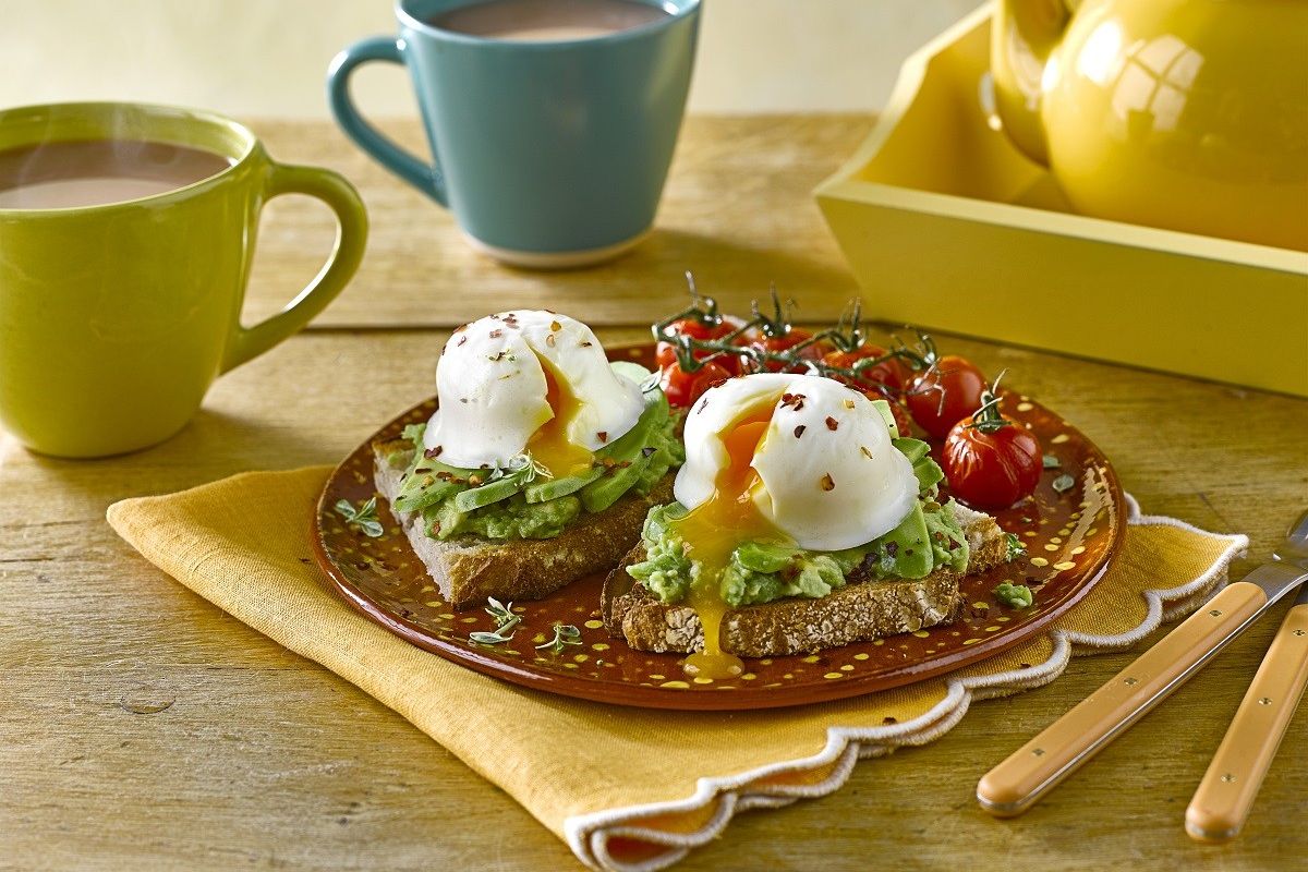 Poached eggs on avocado toast with tomatoes and mugs of tea on table
