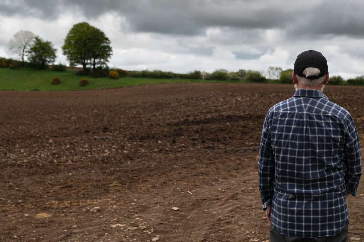 Rear view of a farmer looking at a newly ploughed field in rural Scotland on an overcast day