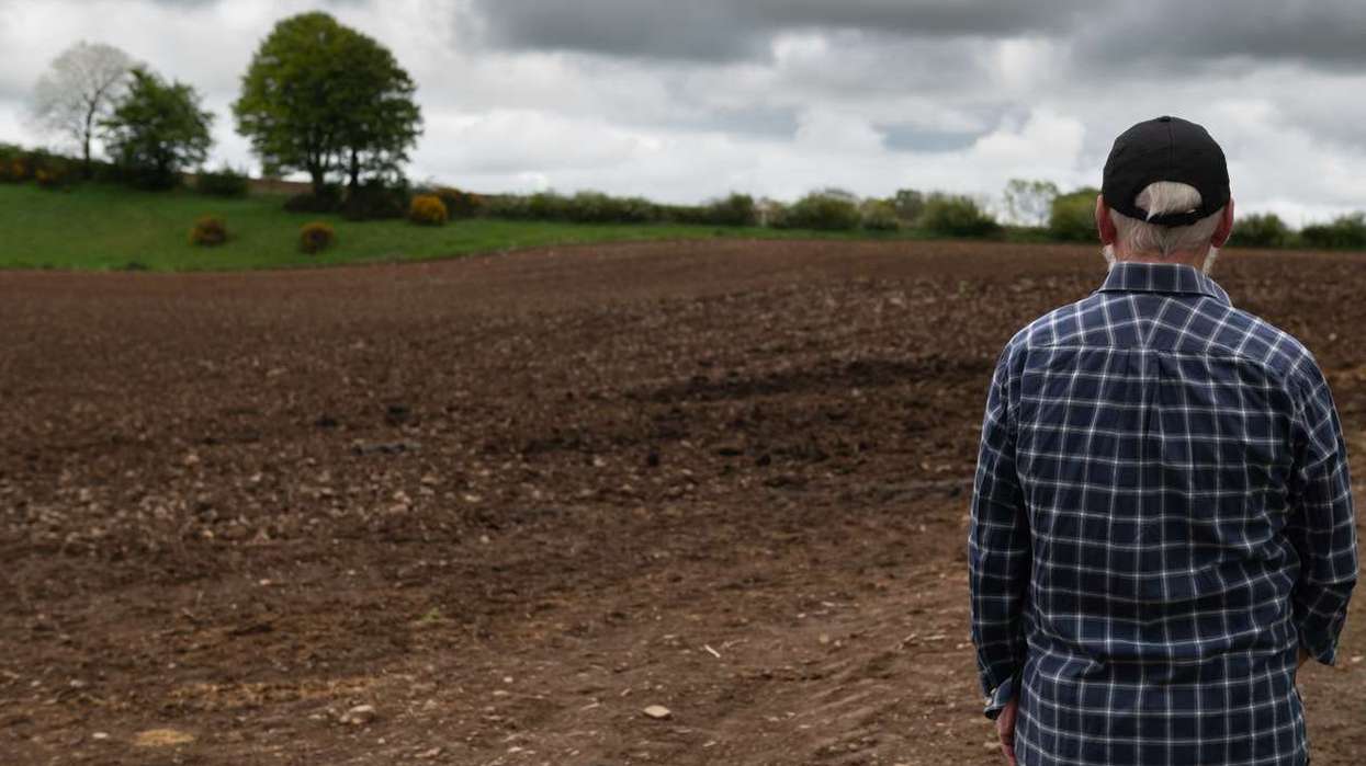 Rear view of a farmer looking at a newly ploughed field in rural Scotland on an overcast day