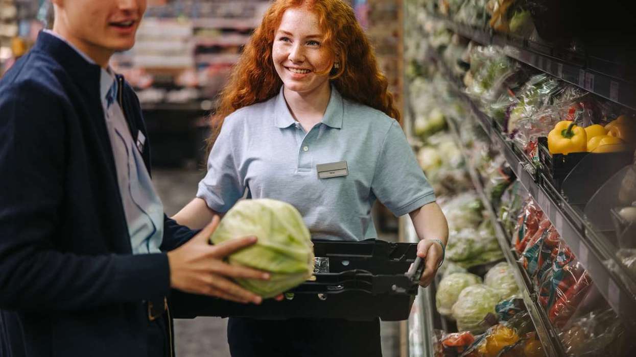 Shop assistants re-stocking fresh vegetables in produce aisle