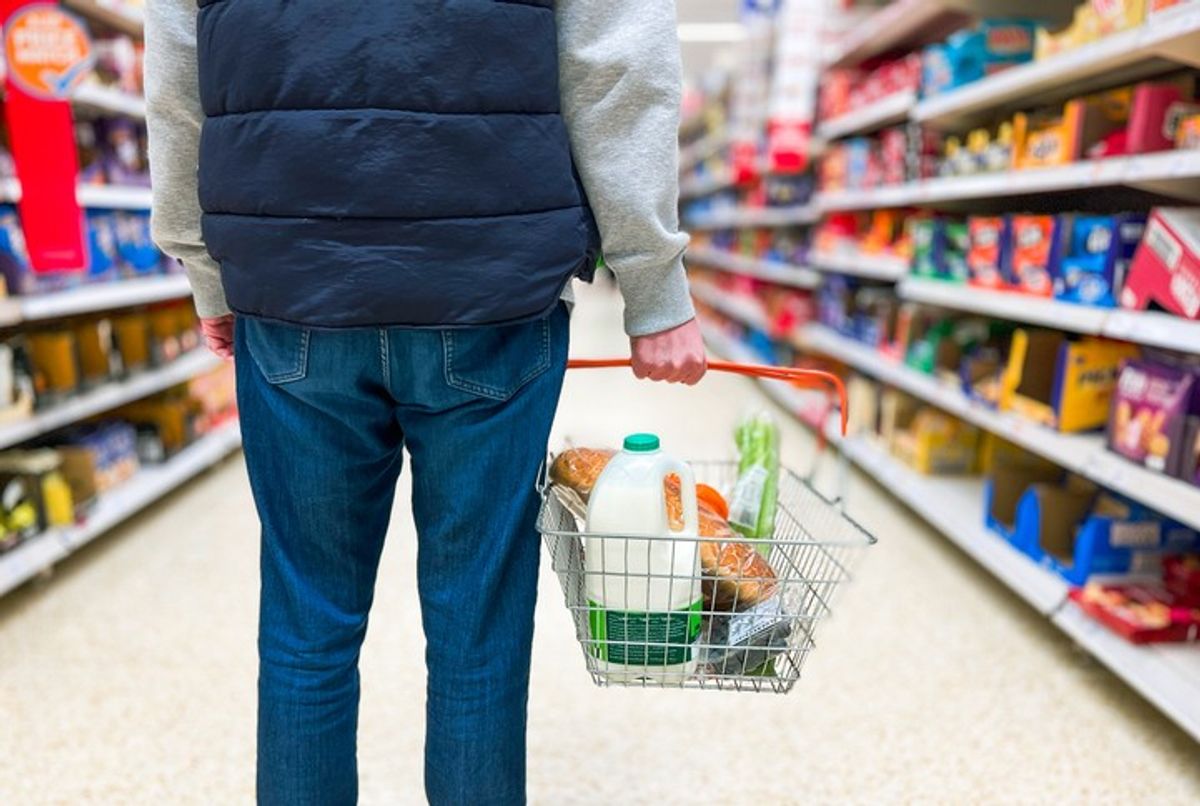 Shopper carries top-up grocery basket in convenience store aisle