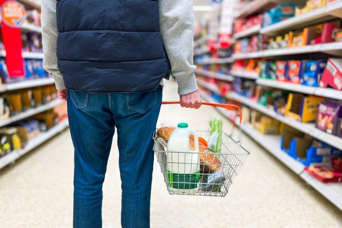 Shopper carries top-up grocery basket in convenience store aisle