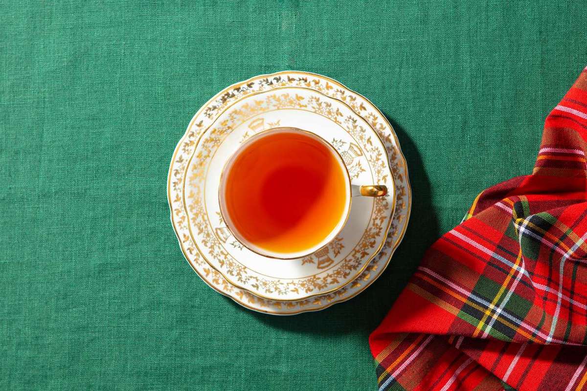 Tea in beige and gold cup on a green cloth with a tartan-style napkin
