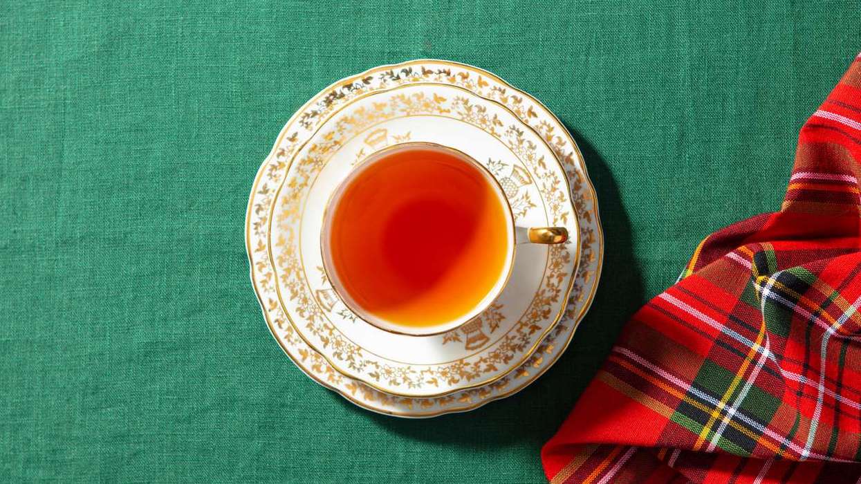 Tea in beige and gold cup on a green cloth with a tartan-style napkin