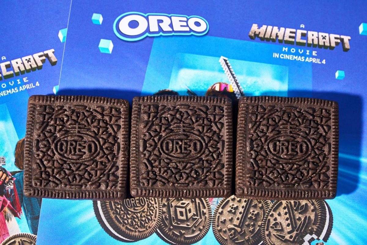 Three square OREO cookies with A Minecraft Movie embossments, placed on a promotional backdrop featuring the OREO logo and A Minecraft Movie poster, highlighting the 2025 partnership and the film’s April 4 release.