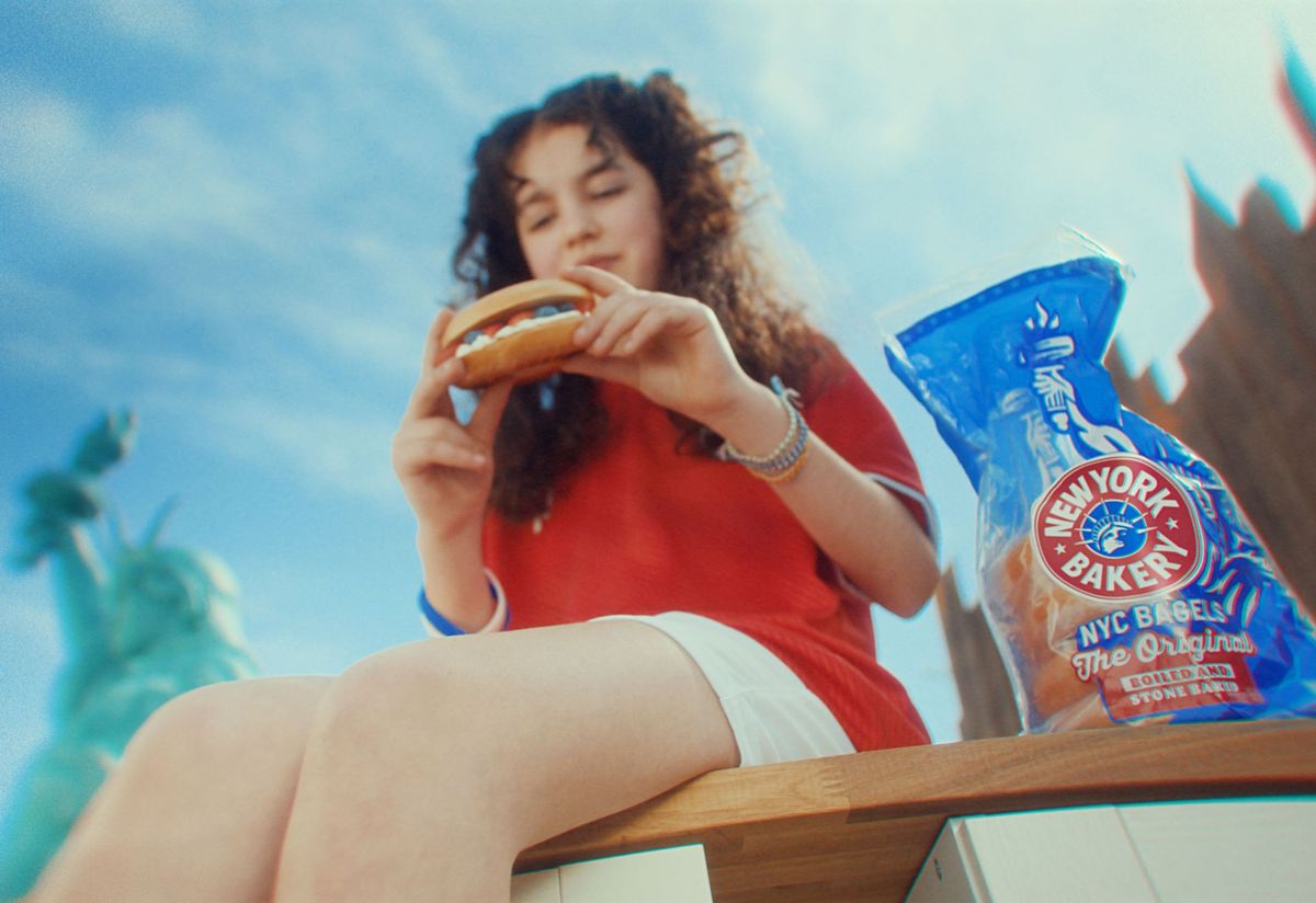 Woman enjoying New York Bakery bagel with Statue of Liberty in background