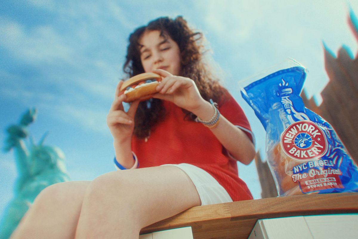 Woman enjoying New York Bakery bagel with Statue of Liberty in background