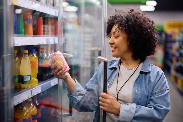 Woman selects chilled soft drink from cooler in convenience store