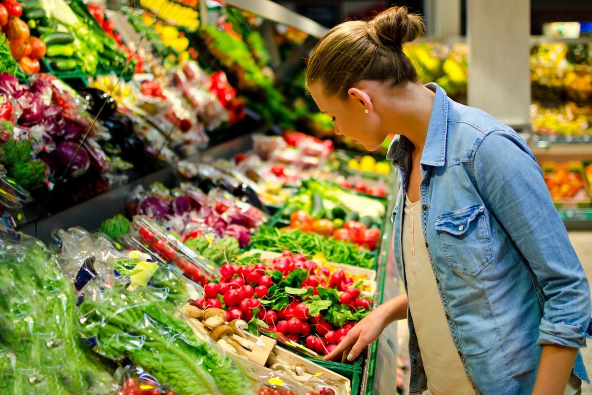 Woman shops for fresh vegetables in supermarket, reflecting shift toward healthier food choices.