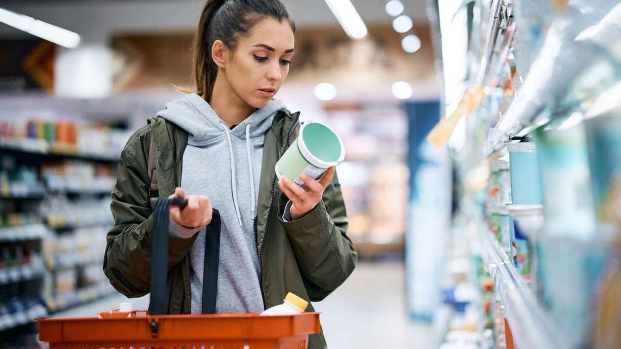 Young woman reading nutrition label while buying diary product in supermarket